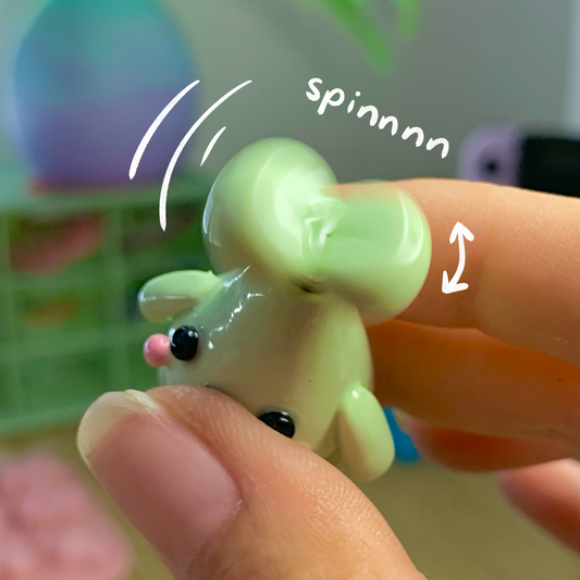 Small green figurine being spun on a finger with text 'spinnnn' against a blurred background.