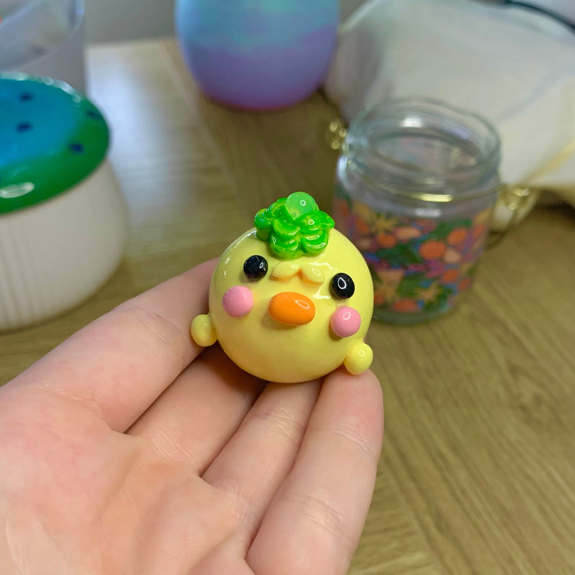 Small yellow bird figurine with a green top held in a hand on a wooden surface.