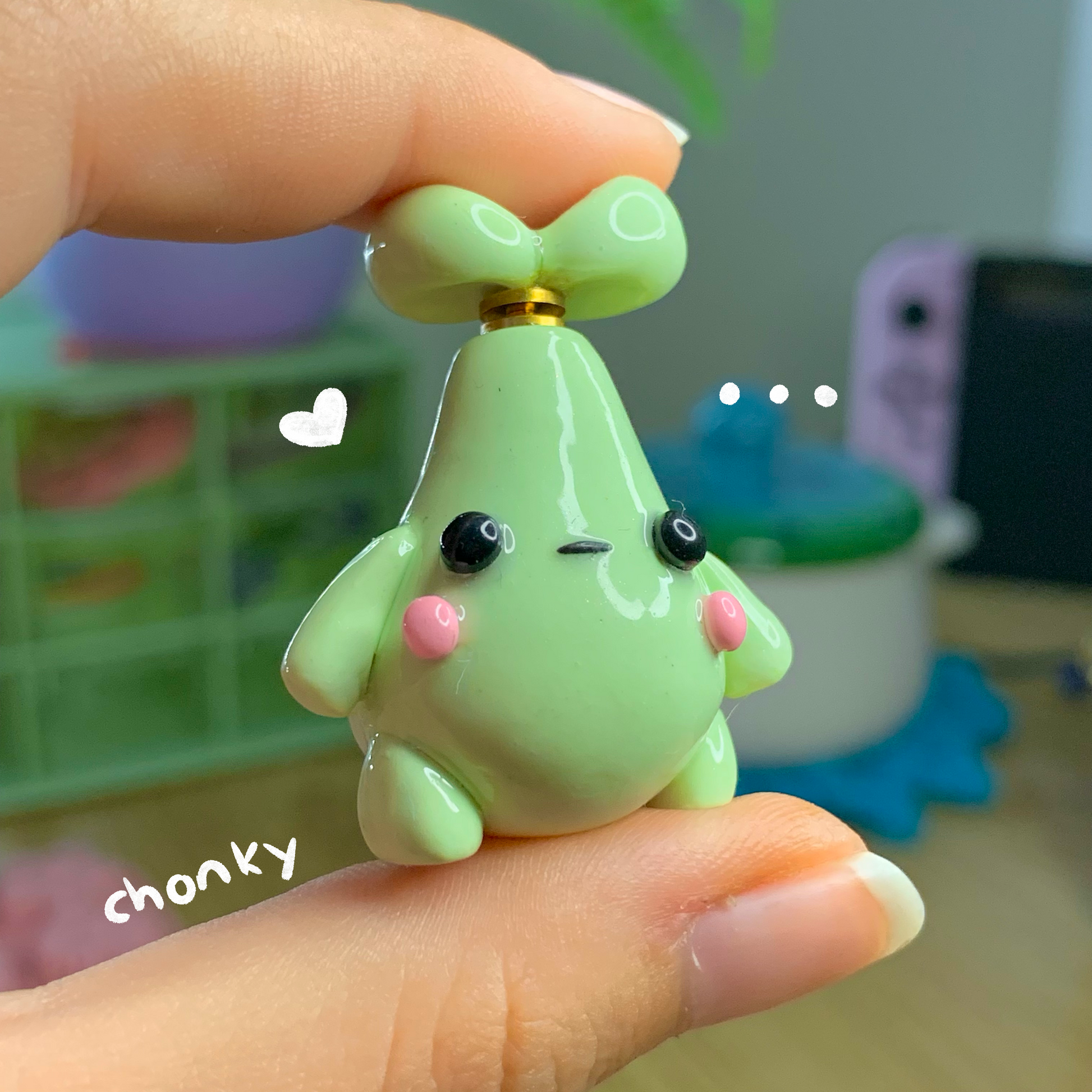 Small green character figurine held in a hand with a blurred background