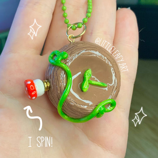 Hand holding a small wooden toy with green beads and a mushroom figure, labeled 'I Spin!'.