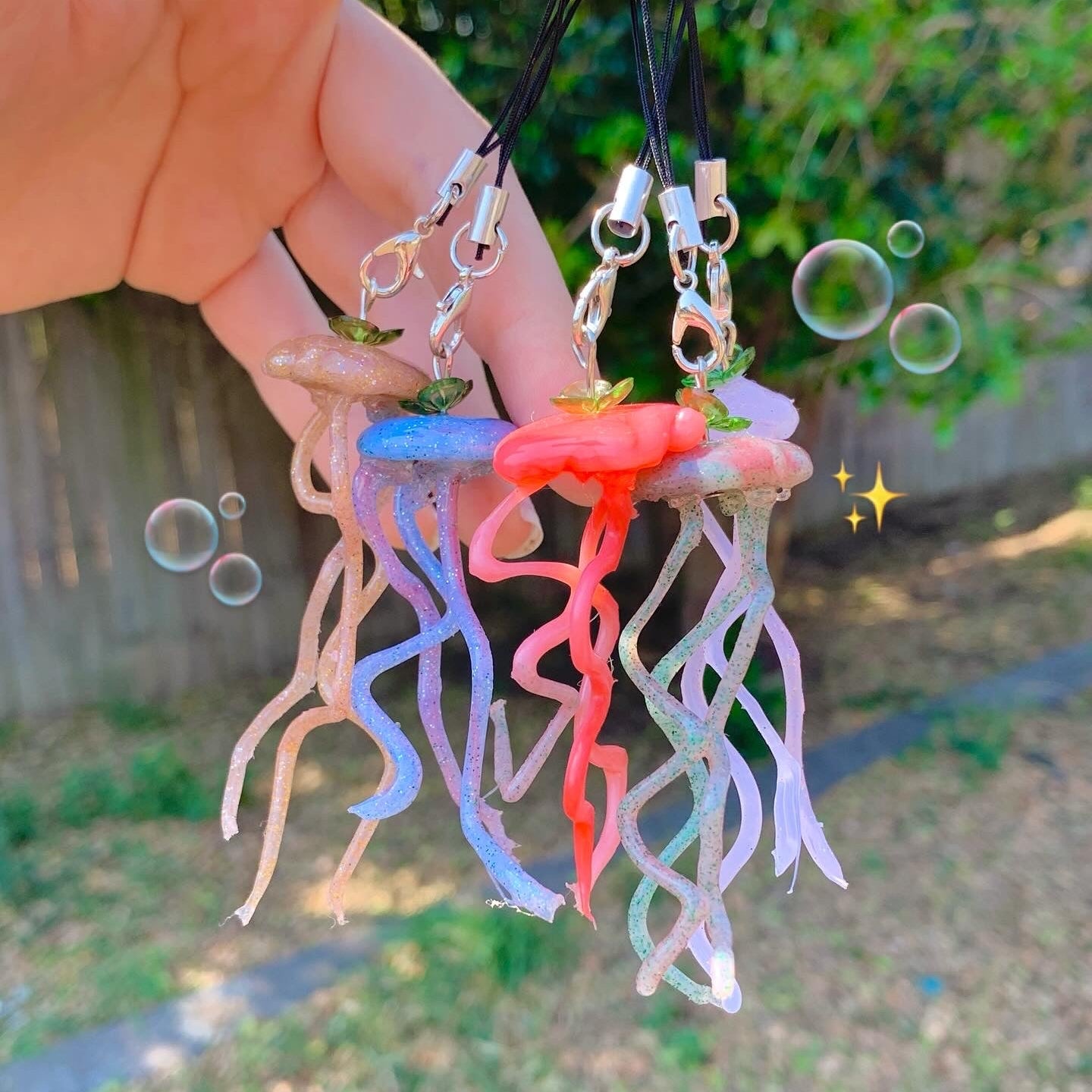 Colorful jellyfish-shaped keychains held by a hand with a blurred outdoor background.