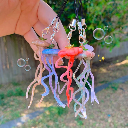 Colorful jellyfish-shaped keychains held by a hand with a blurred outdoor background.