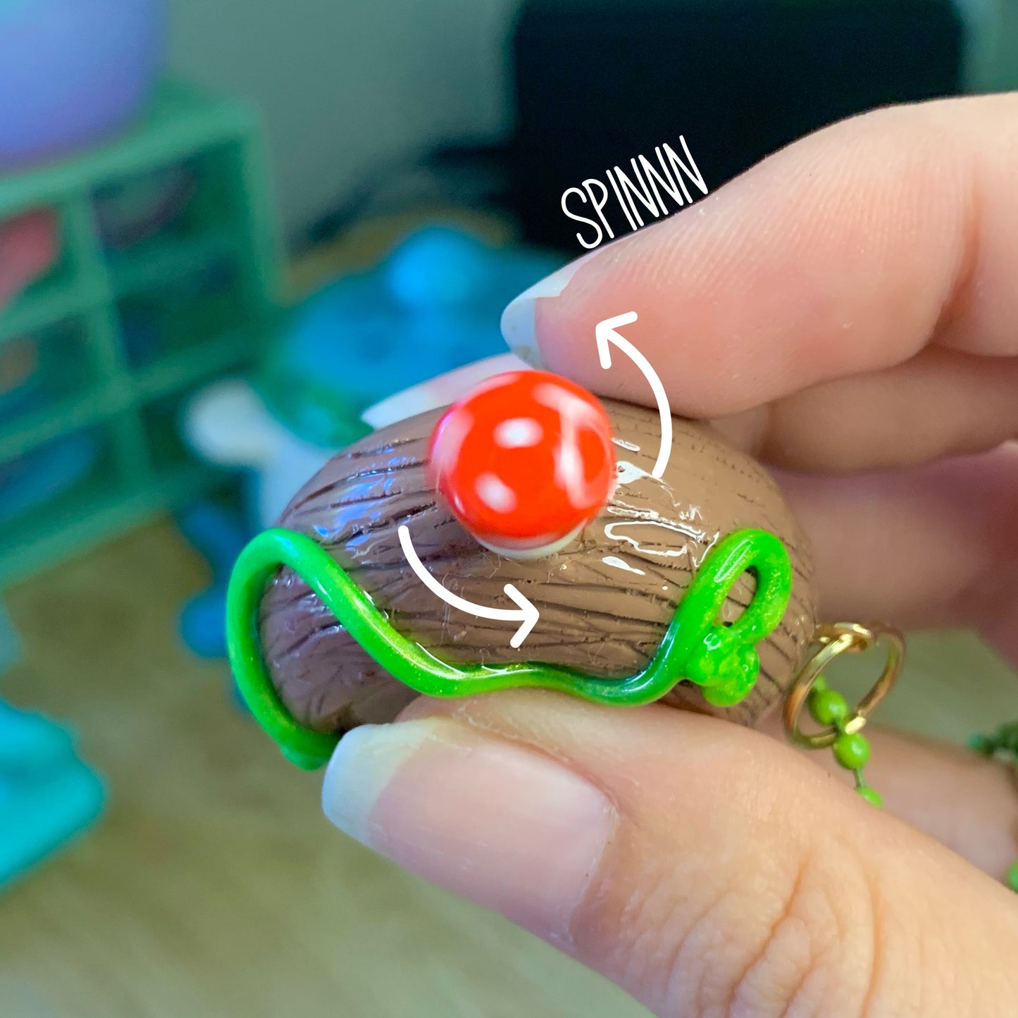 Hand holding a small toy figure with a red ball on top, labeled 'SPINNA'.