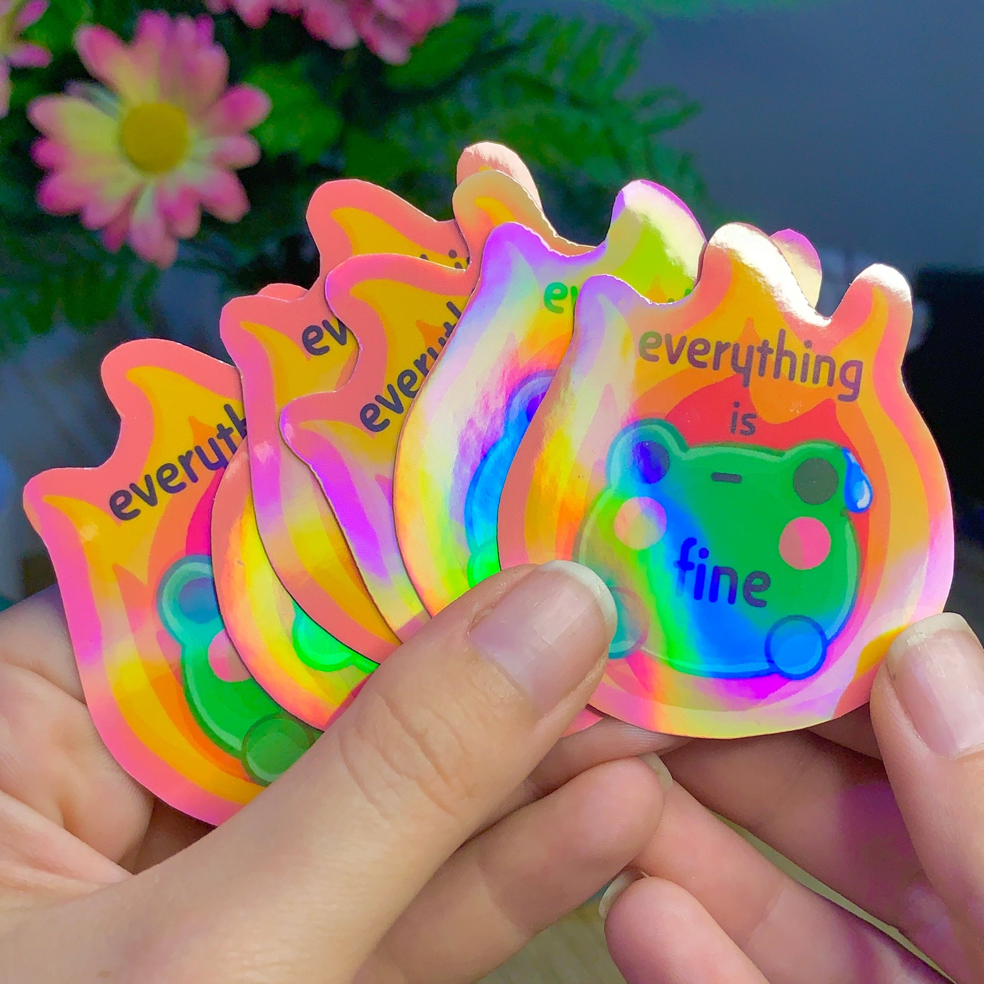 Colorful 'everything is fine' sticker held by hands with a blurred floral background