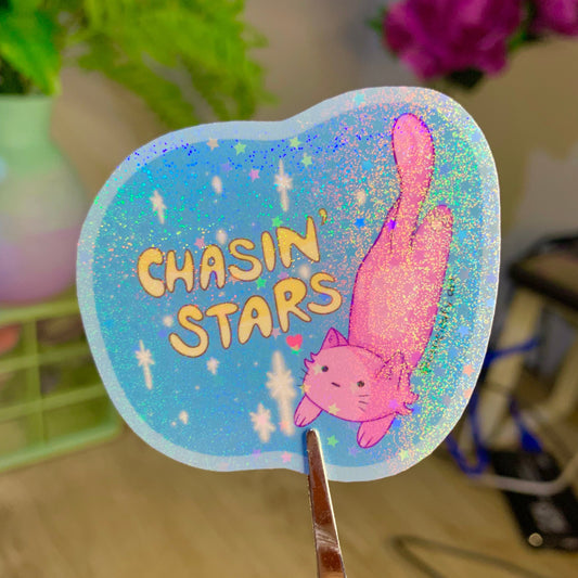 Sticker with 'Chasin' Stars' text and a pink cat illustration held by scissors.