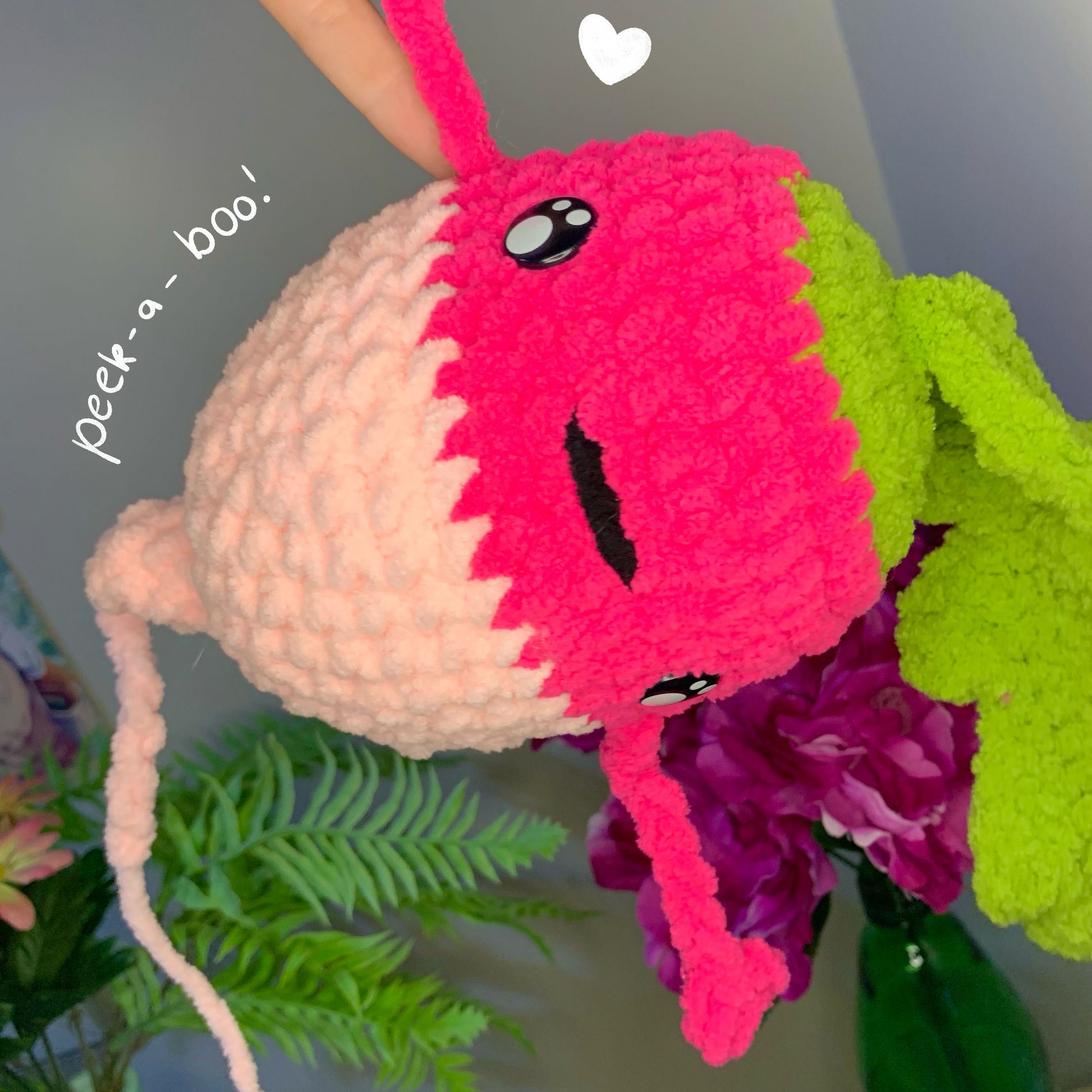 Handmade plush toy with a pink and white face peeking out from behind green leaves and a bottle.