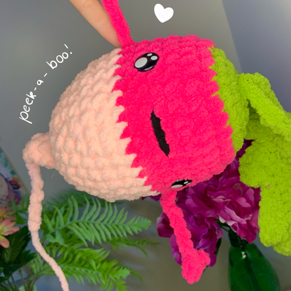 Handmade plush toy with a pink and white face peeking out from behind green leaves and a bottle.