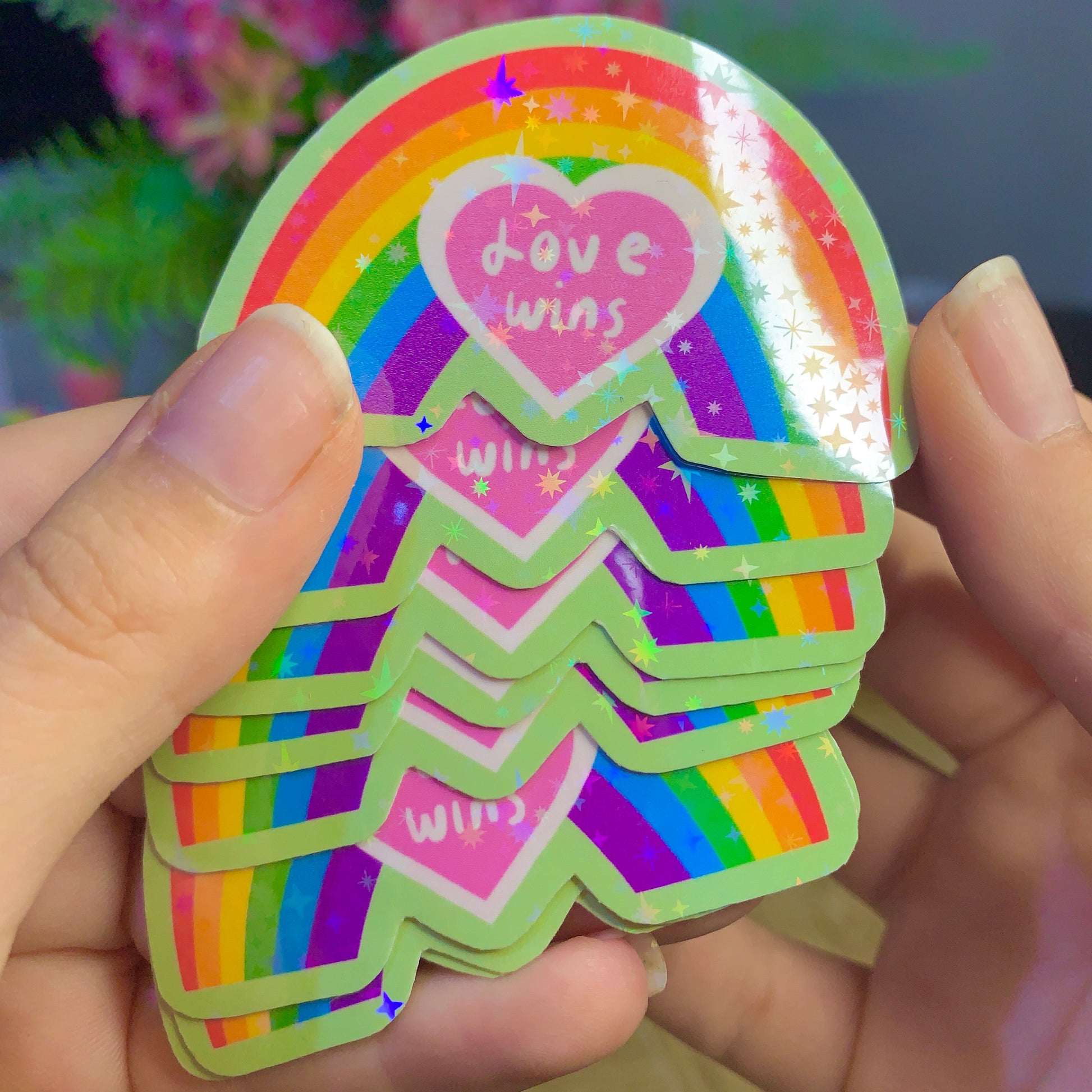Stack of rainbow-colored stickers with 'Love wins' text held by a person.