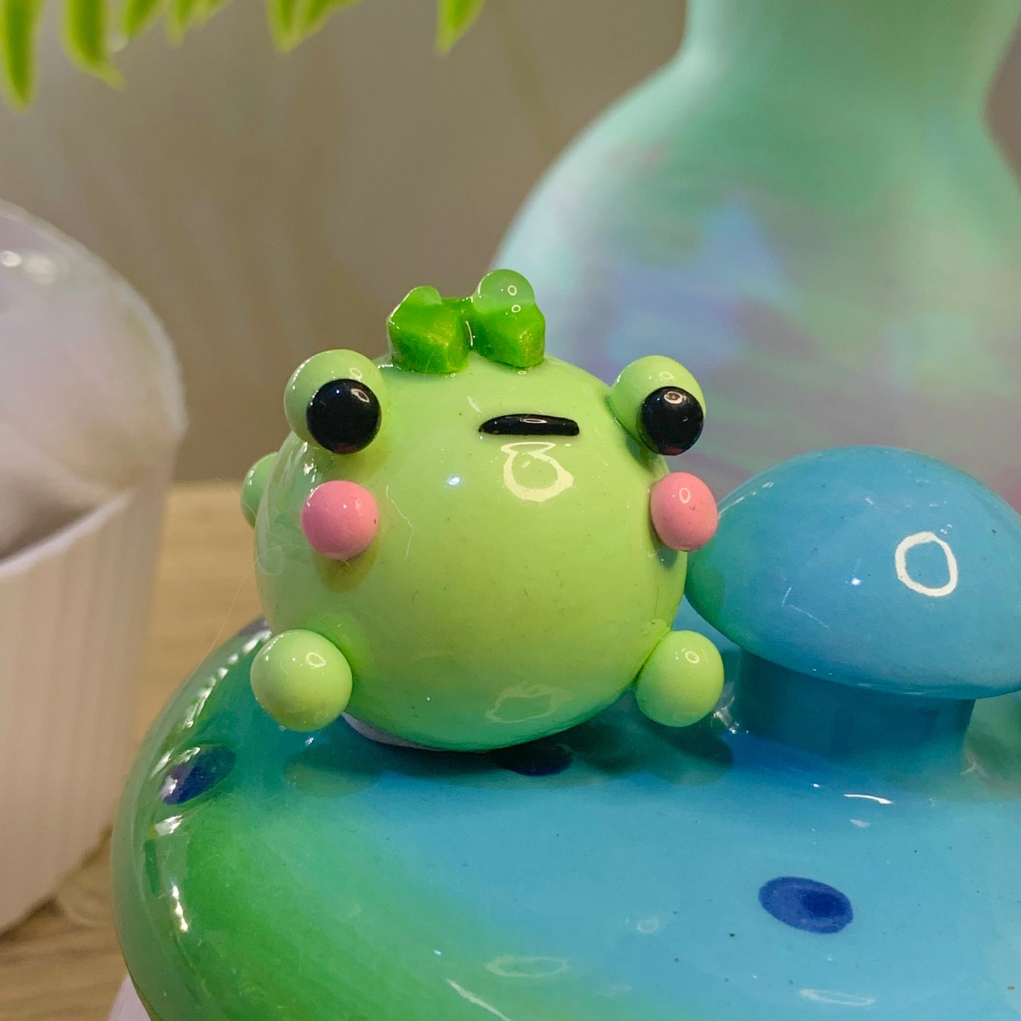 Green frog with black eyes and pink cheeks on a blue and green base