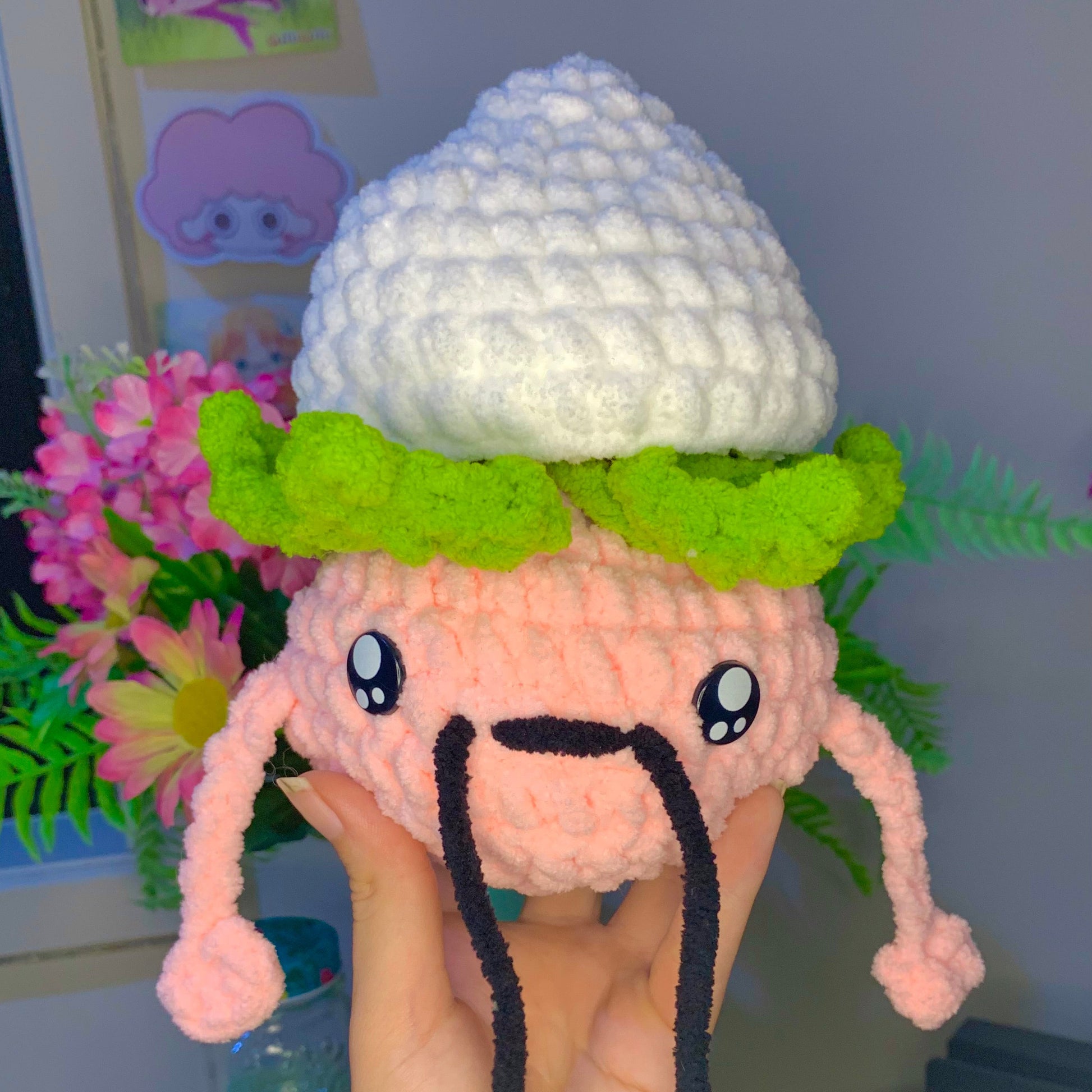 Plush toy resembling a cartoon character with a white hat and green leaves, held by a person.