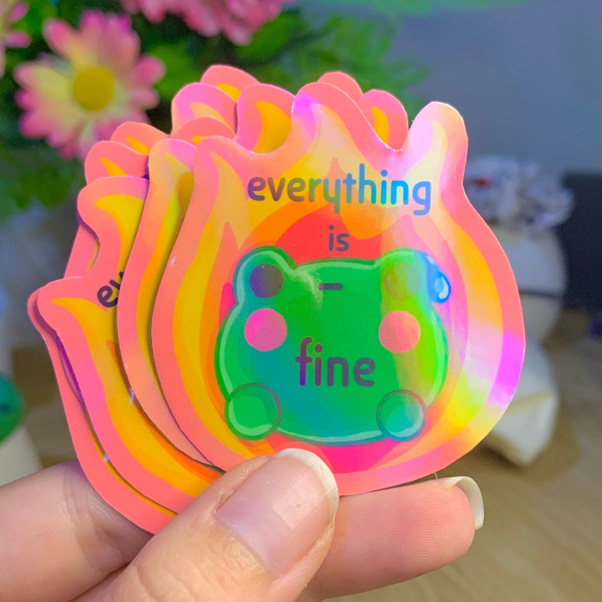 Colorful card with 'everything is fine' text held by a hand, with flowers in the background.